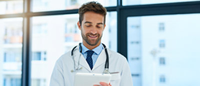 A medical practitioner wearing a stethoscope smiling while looking at their device.