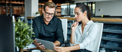 Two people looking at a Surface in an office space with a plant in the foreground.