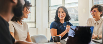 A diverse group of coworkers collaborate in an office space while one takes notes on his laptop.