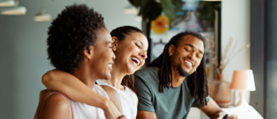 Diverse group of friends laugh and look at photos on a cellphone over coffees in a cafe.