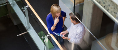 Two people in discussion, one has a device in their hand, the image is captured from above.