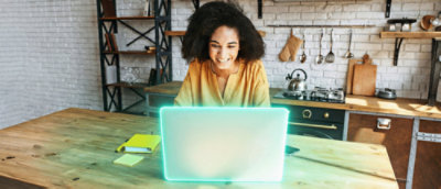 Individual using a laptop at a kitchen table in a home setting, representing remote monitoring or digital access to energy services through connected technology.