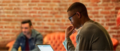Un homme assis, regardant un ordinateur portable, la main sur le menton.