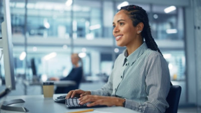 A woman sits at a desk, focused on her computer and keyboard, working in a professional environment.