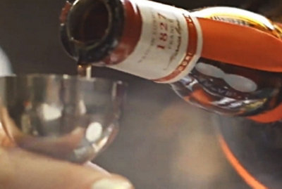 A person pouring liquid into a glass with a close-up of a bottle visible.