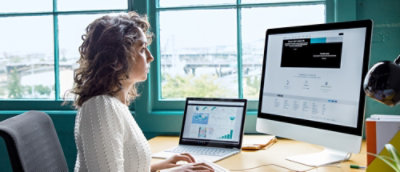 A person sitting at a desk with a laptop and a visible computer screen.
