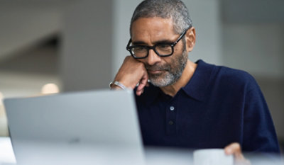 A man wearing glasses is looking at a laptop.