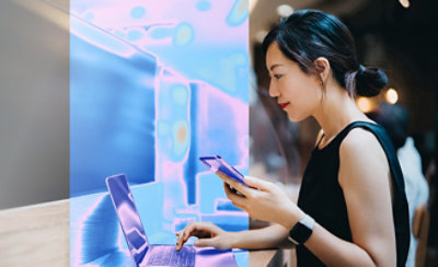 A women holding mobile and looking into laptop.