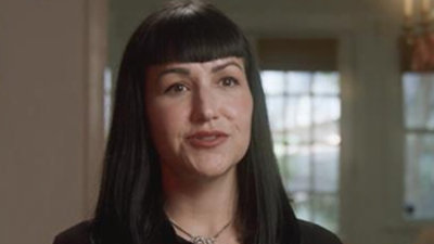 A close-up of a woman with black hair and bangs wearing a necklace.
