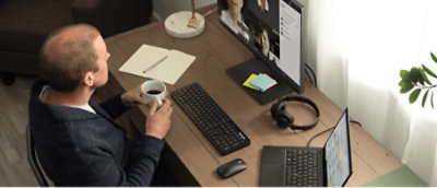 コンピューターとコーヒーのある机に向かって座っている人