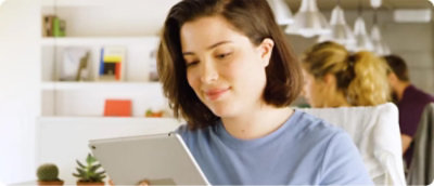 Person holding a tablet in an office environment with other individuals working in the background.