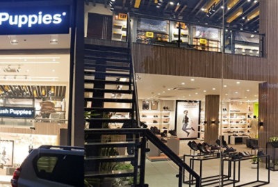 A storefront of a hush puppies store in an urban setting at night, with a customer exiting and an illuminated sign above.