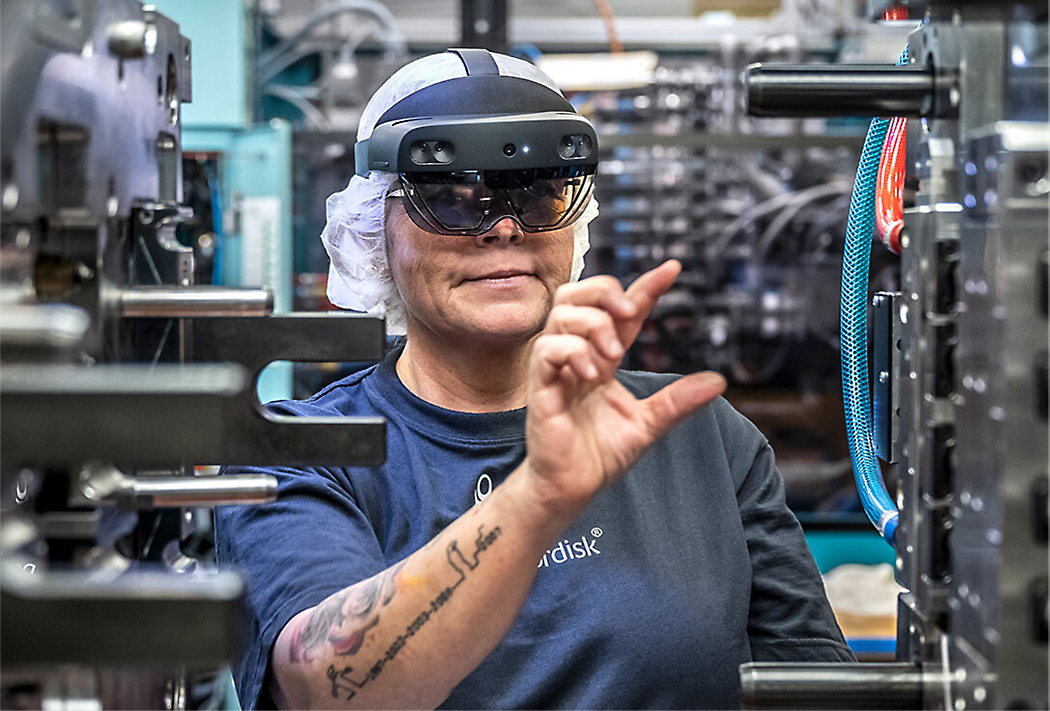 A worker wearing a head-mounted augmented reality device inspects machinery in an industrial setting.