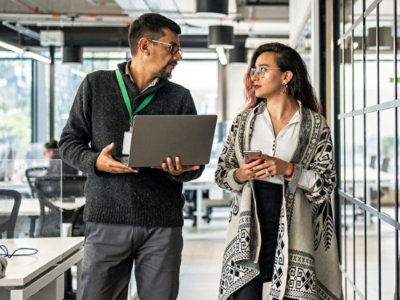 在现代化的办公室中，两位专业人士正在讨论，一位手持笔记本电脑，另一位手持智能手机。