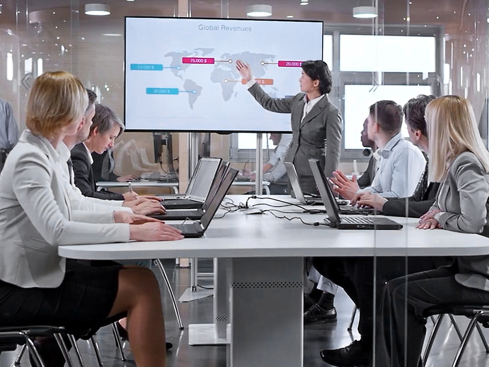 Eine professionelle Geschäftspräsentation in einem modernen Büro, bei der ein Referent auf einen Bildschirm zeigt, der globale Umsätze anzeigt