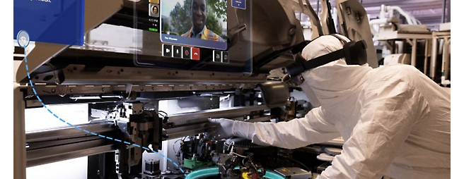 A technician in a cleanroom suit operates advanced manufacturing equipment in a high-tech facility.