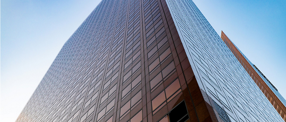 Low-angle view of two modern glass skyscrapers converging under a clear blue sky.