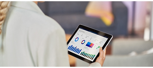 Bir ofis ortamında veri analizini gösteren renkli grafikler ve çizelgelerin görüntülendiği tableti kullanan bir iş kadını.