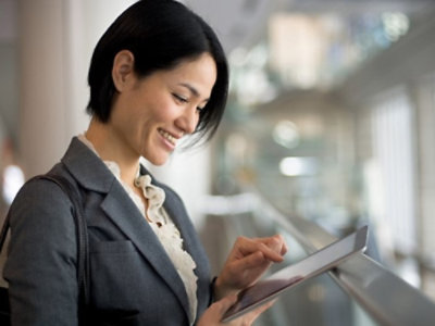 A smiling asian businesswoman using a tablet in a modern office setting.