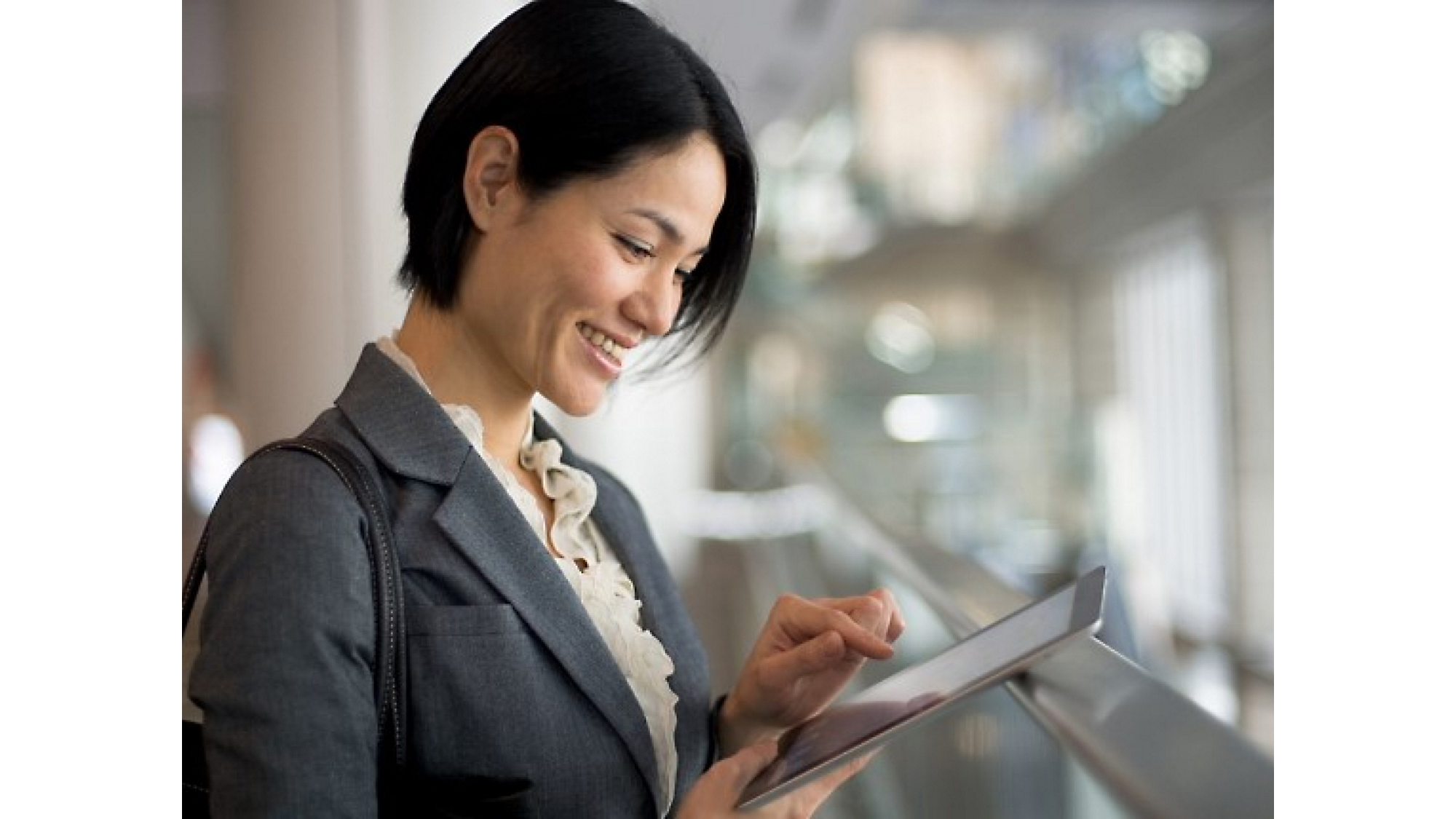Uma empresária asiática sorrindo usando um tablet em um ambiente de escritório moderno.