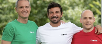 Three men standing together, one in a red shirt, middle person in a white shirt and the other in a green shirt, with partial text fløwe visible.