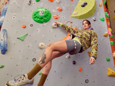 A person wearing climbing gear scales an indoor rock climbing wall with various colorful holds.