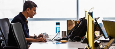 Un homme assis à un bureau, concentré sur son ordinateur portable, entouré d'un espace de travail bien rangé.
