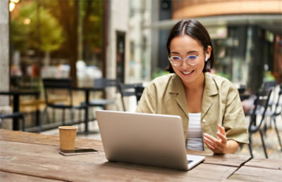 A woman wearing glasses and a tan jacket using a laptop.