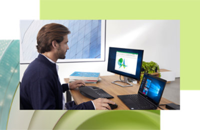 Man working on a desktop and laptop at a modern office desk, analyzing data on a screen with graphical charts.