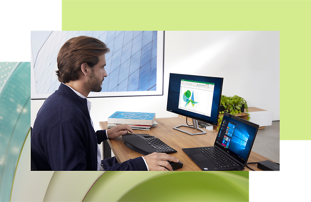 Hombre trabajando en un equipo de escritorio y portátil en un escritorio de oficina moderno, analizando datos en una pantalla con gráficos.
