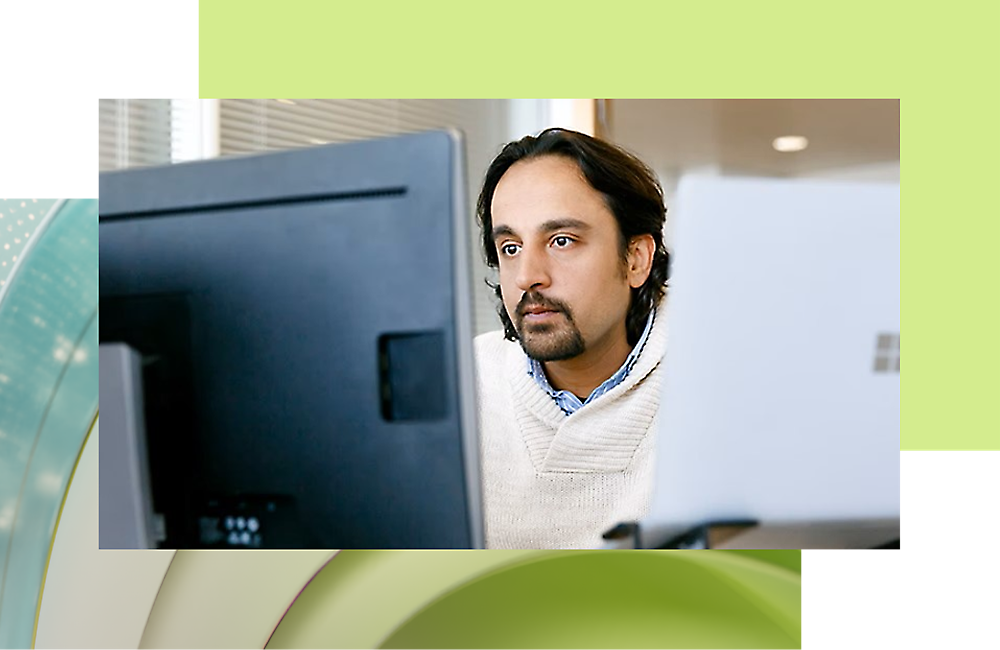 Чоловік із волосся середньої довжини зосереджено працює на своєму комп’ютері в офісі.