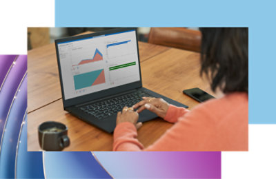 บุคคลที่โต๊ะไม้กําลังวิเคราะห์แผนภูมิข้อมูลบนแล็ปท็อป โดยมีสมาร์ทโฟนและถ้วยกาแฟอยู่ใกล้ๆ