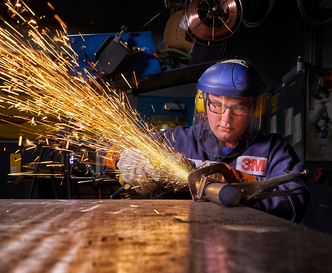 A welder in protective gear focuses on his work as sparks fly from the metal he is grinding.