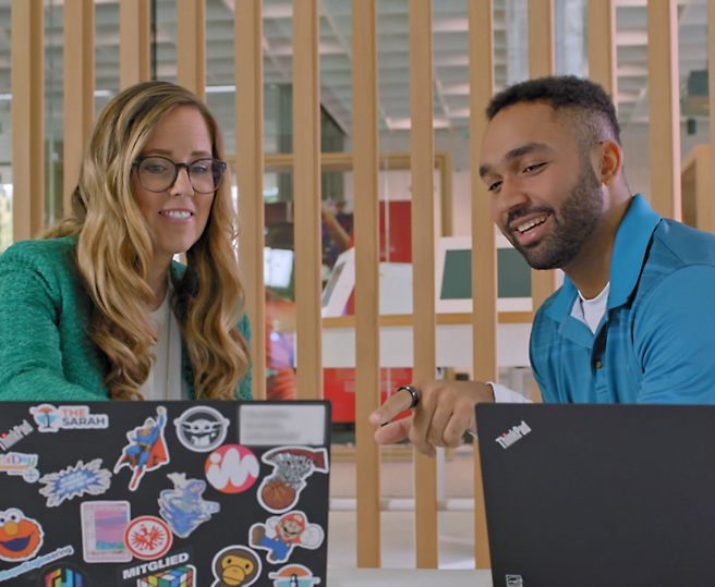Dois profissionais falando sobre trabalho em laptops em uma configuração moderna do escritório.