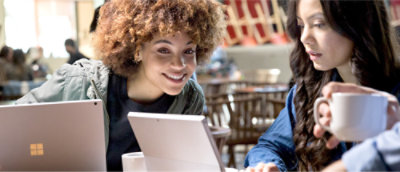 两个人坐在咖啡馆的一张桌子旁，各自用笔记本电脑工作。一个人微笑地看着另一个人的屏幕。