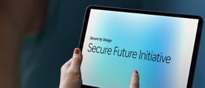 画面を指す指でタブレットを持っている人。青色の背景に「Secure by Design Secure Future Initiative」というテキストが表示されています。
