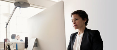 明るくモダンなオフィスでデスクトップ コンピューターで作業しているフォーマルな服を着ている女性。