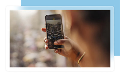 A person holds a smartphone, capturing a photo of a crowded street with heavy traffic.