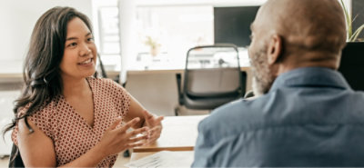 Two coworkers having a one‑on‑one discussion across a desk in an office.
