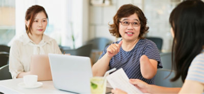 People seated at a table, discussing documents with a laptop during a meeting.