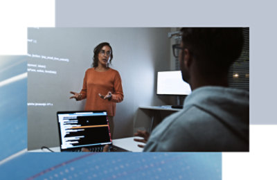 Small group discussion in a workspace, reviewing code displayed on a screen.