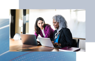 Two coworkers seated at a table, collaborating on laptops during a discussion.
