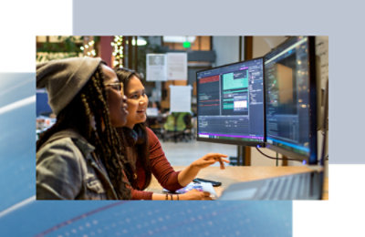Two coworkers reviewing code together on dual monitors in a shared workspace.