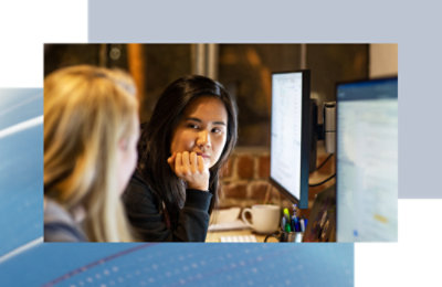 Two coworkers at desks, reviewing information side by side on monitors.