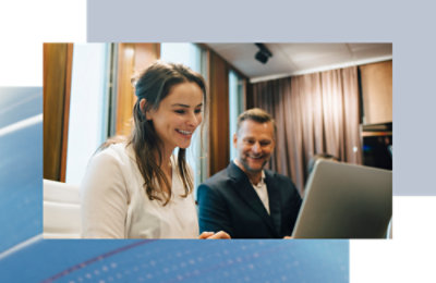 Two coworkers seated side by side, collaborating on a laptop in a meeting room.
