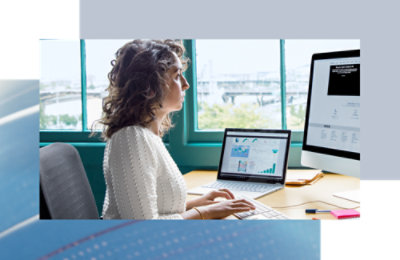 Person working at a desk, viewing charts and data on dual computer screens.