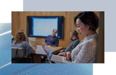 Person using a laptop while others meet at a conference table in the background.