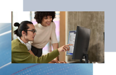 Two coworkers collaborating at a desktop computer, reviewing content on screen.