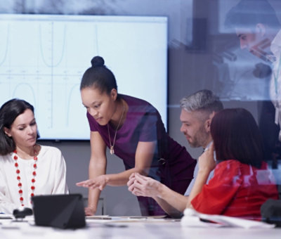 A diverse group of professionals discussing around a laptop in a modern office setting.