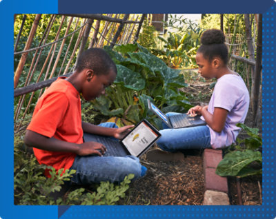 Um menino e uma menina sentados em um jardim usando notebooks.